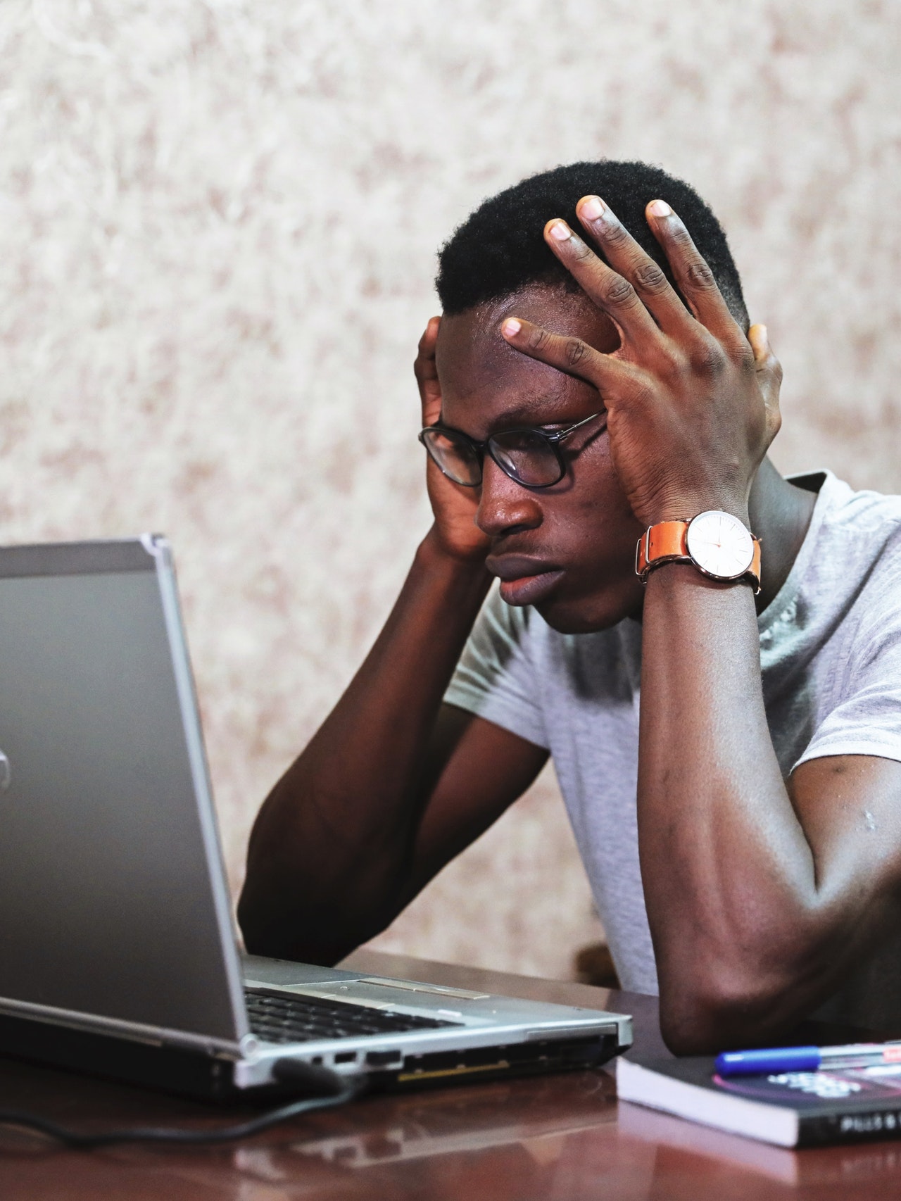 Take time to de-stress before finals Man holds hands on head while looking at laptop