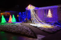 White Christmas tree in window of a house decorated with holiday lights