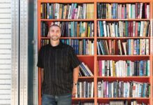 Observing America’s pandemic response from abroad Michael stands in front of bookcase