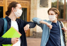 Back to school in the time of COVID-19 Young students bump elbows while wearing masks