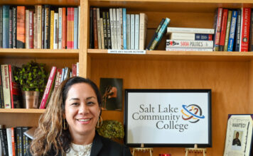 SLCC’s first chief diversity officer accepts new job in Hawaii Dr. Kinikini stands next to SLCC sign on bookshelf