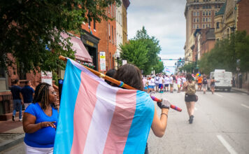 The impact of deadnames Person walking with transgender pride flag during Baltimore Pride event