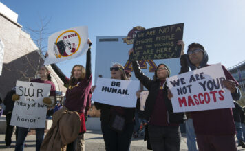 Decades of activism helping to eliminate Native American mascots Multiple protesters hold signs denouncing Washington Redskins
