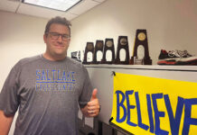 Ready to run: New SLCC cross country team finds its coach Isaac Wood gives a thumbs-up while standing next to a shelf of NCAA trophies