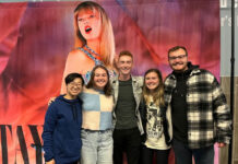 Students chime in on Taylor Swift’s ‘The Eras Tour’ movie Five people stand together for a group photo in front of Taylor Swift movie art