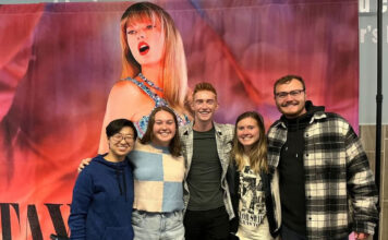 Students chime in on Taylor Swift’s ‘The Eras Tour’ movie Five people stand together for a group photo in front of Taylor Swift movie art