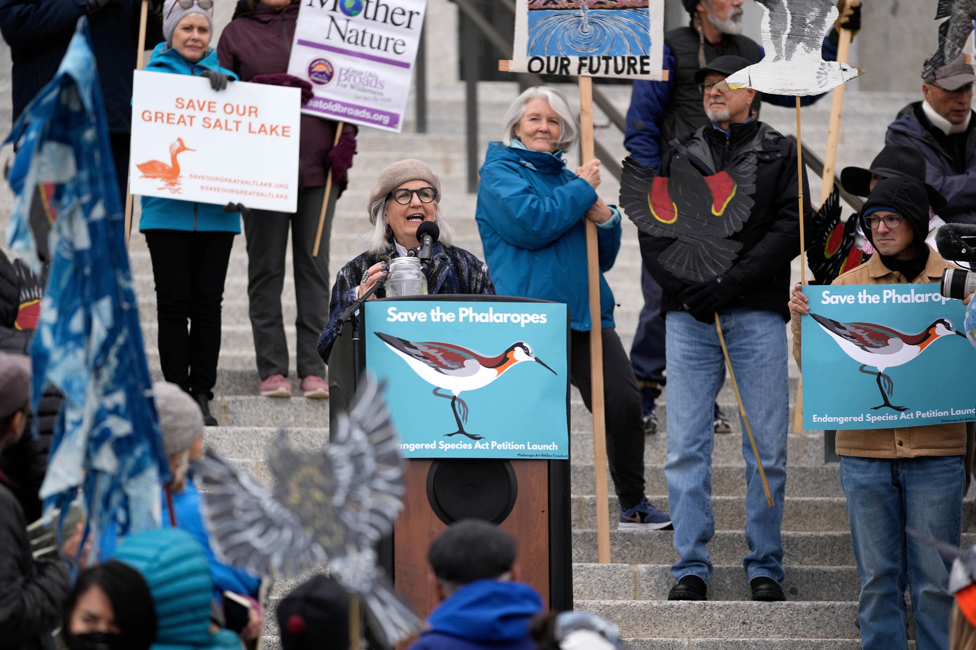 Terry Tempest Williams standing at podium while surrounded by activists