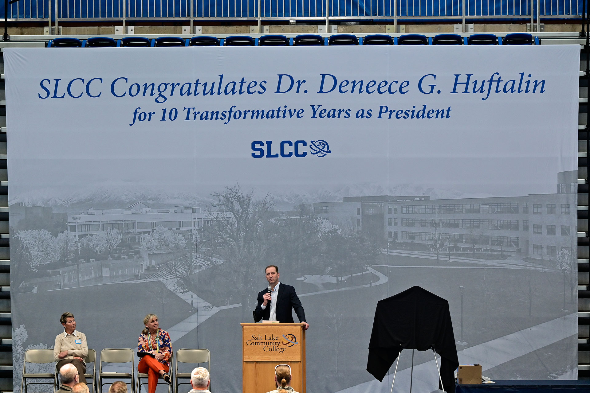 People on stage underneath a large banner that reads "SLCC Congratulates Dr. Deneece G. Huftalin for 10 Transformative Years as President"