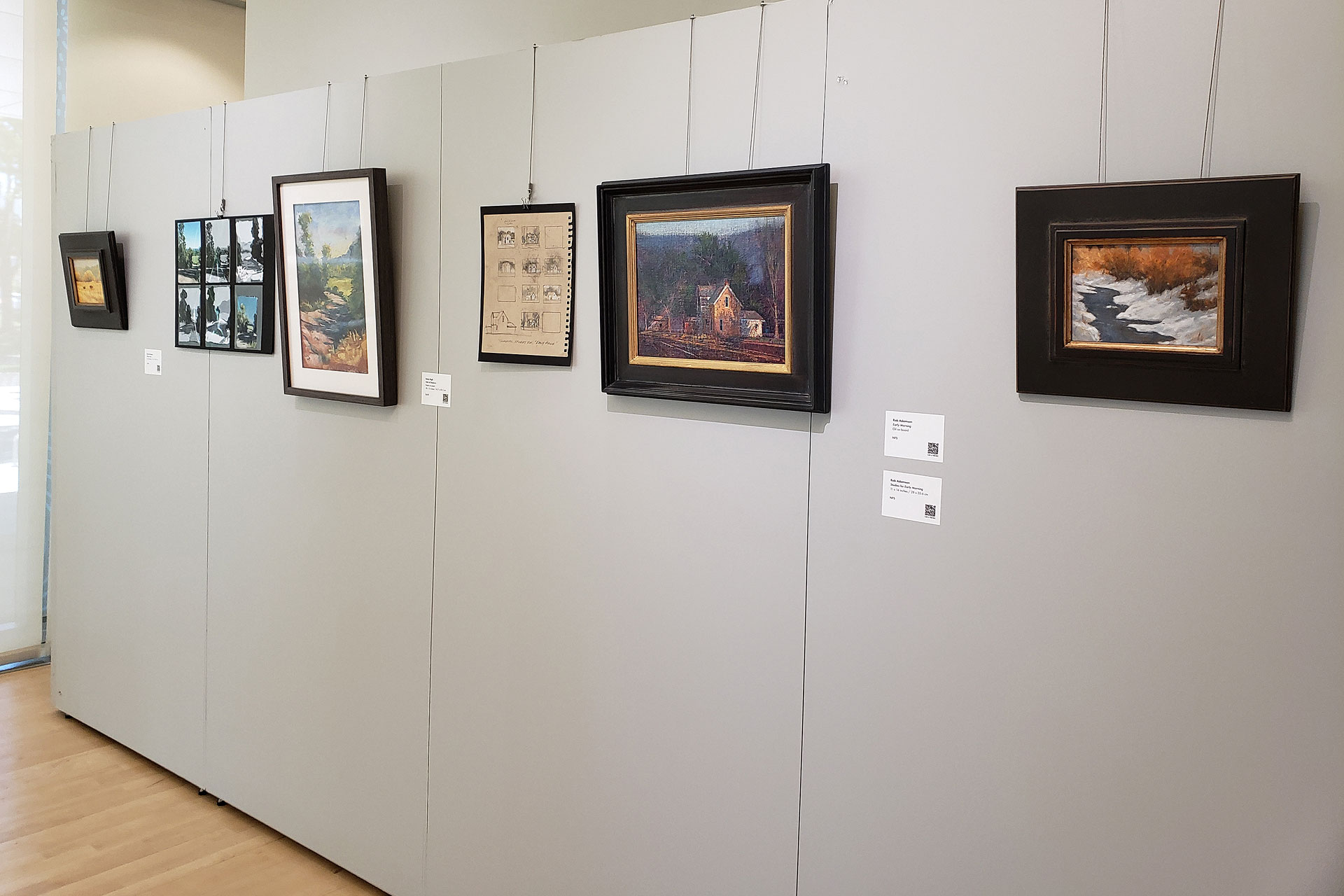 A row of paintings displayed on a wall in a gallery