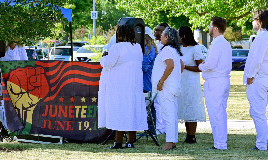 Singers wearing white clothing stand in shade before performance
