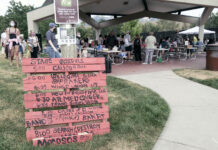 Alternative Pride festival in Salt Lake City promotes community over corporations A wood pallet painted red with event schedule painted in black lettering, with an open air market in background