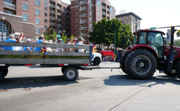 Families celebrate new experiences and classic traditions on Pioneer Day Tractor pulling trailer filled with people on a parade route