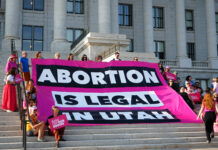Utah Supreme Court decision to uphold block on abortion trigger law elicits many viewpoints Dozens of people sit on capitol building steps with a sign that reads "abortion is legal in Utah"