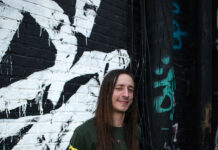 SLCC music grad stays busy in the local scene Sam Jessing standing in front of graffiti-covered wall