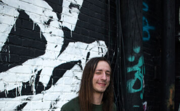 SLCC music grad stays busy in the local scene Sam Jessing standing in front of graffiti-covered wall