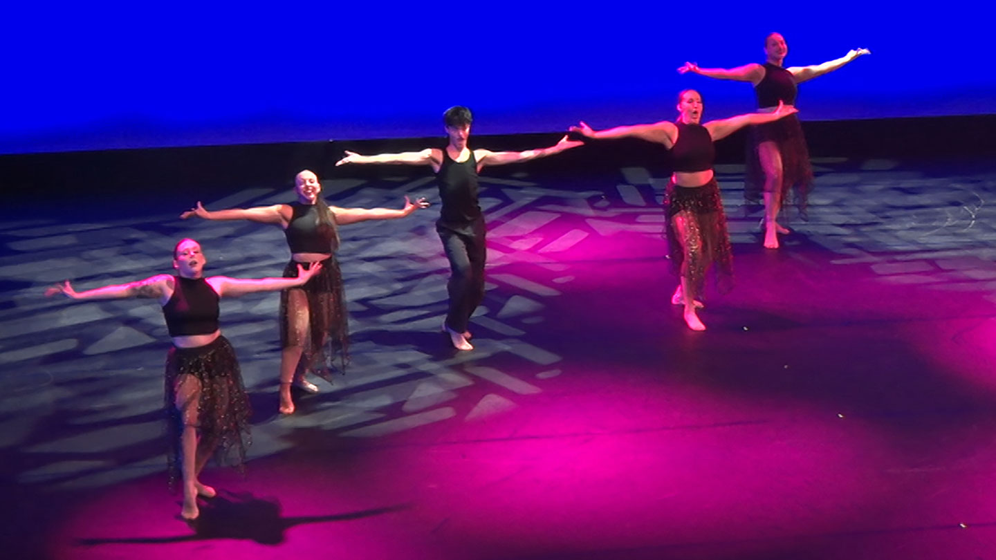 Five dancers perform a routine on stage