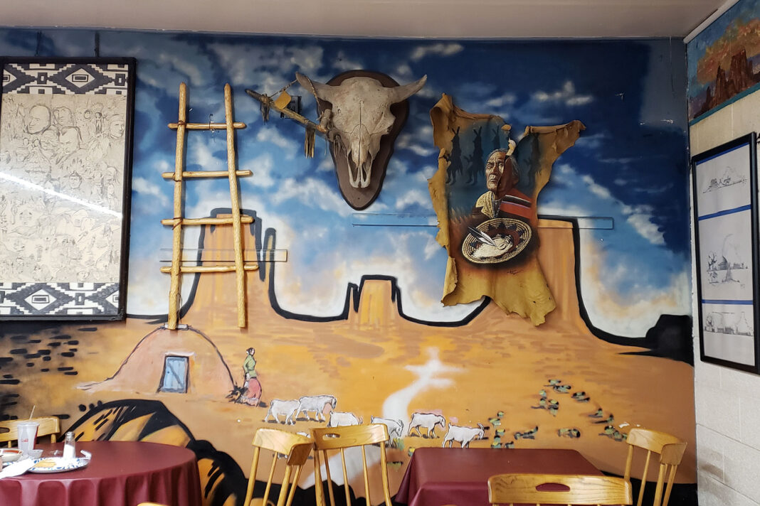 Native American artifacts hanging on a wall painted with a desert mural scene