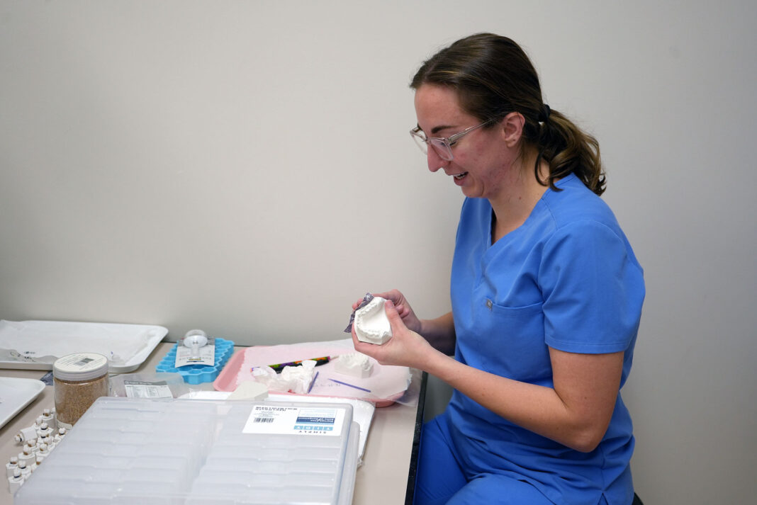 Dental hygiene student wearing blue scrubs and working in a lab