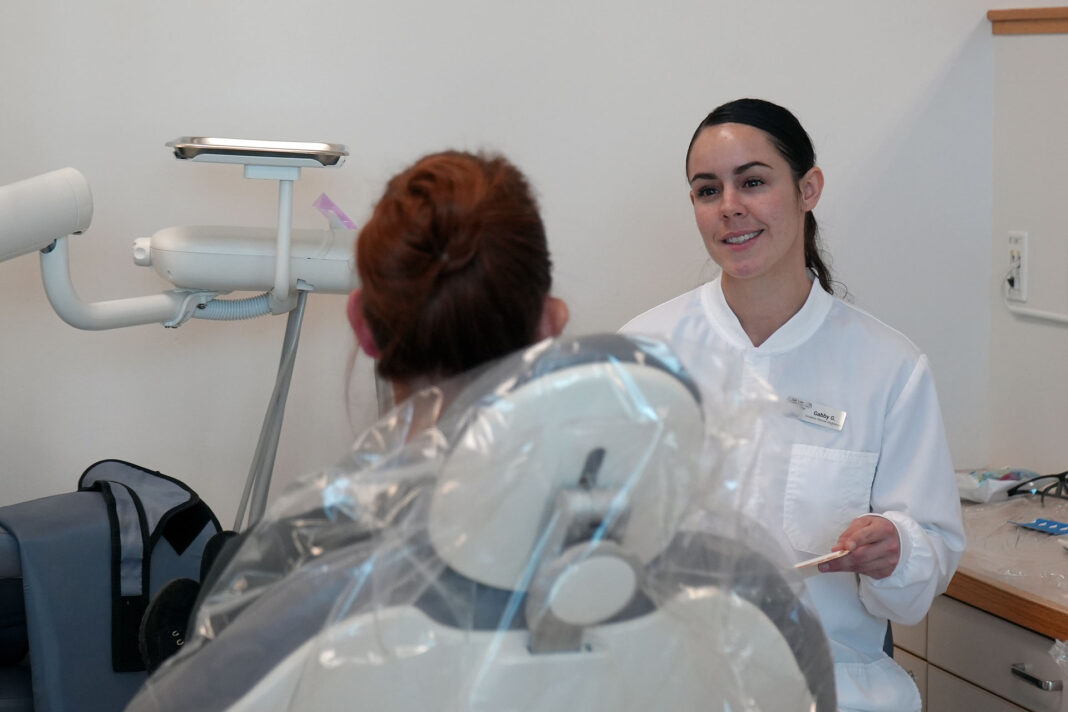 Dental hygiene student talking with a patient who is seated in dental chair