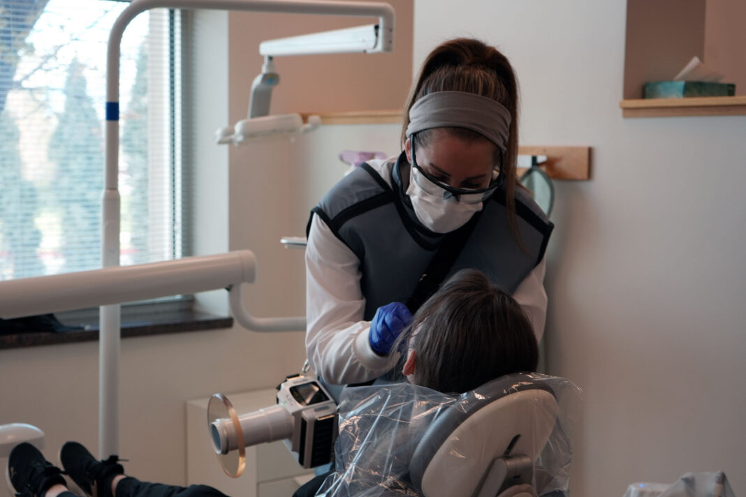 Dental hygiene student wearing lead vest and PPE while administering a test