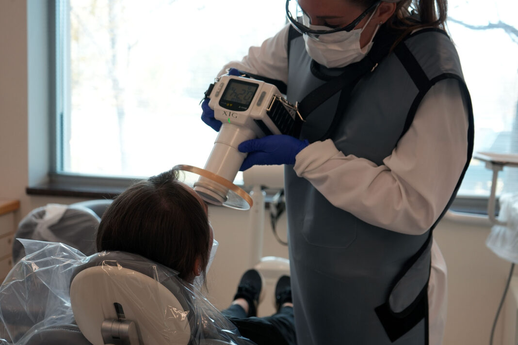 Dental hygiene student wearing PPE while using a handheld x-ray device