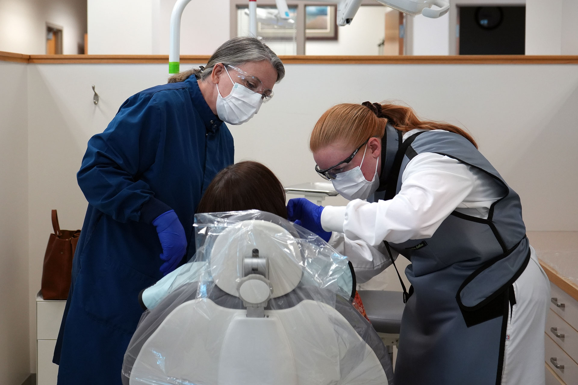 Dental hygiene student preparing to x-ray a patient's teeth while instructor observes