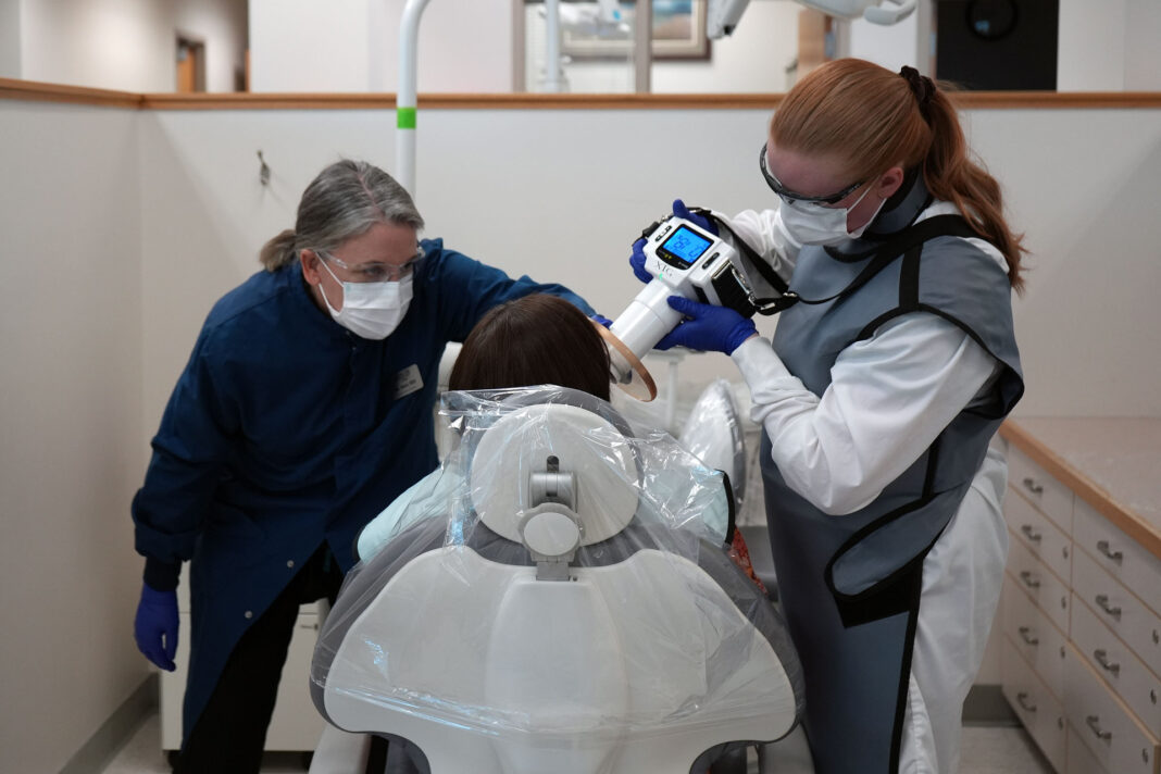 Dental hygiene student using a handheld x-ray device while instructor observes