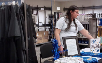 Cuenta regresiva para la inauguración de SLCC: Celebrando un nuevo capítulo Avelina working at a table surrounded by graduation items for sale