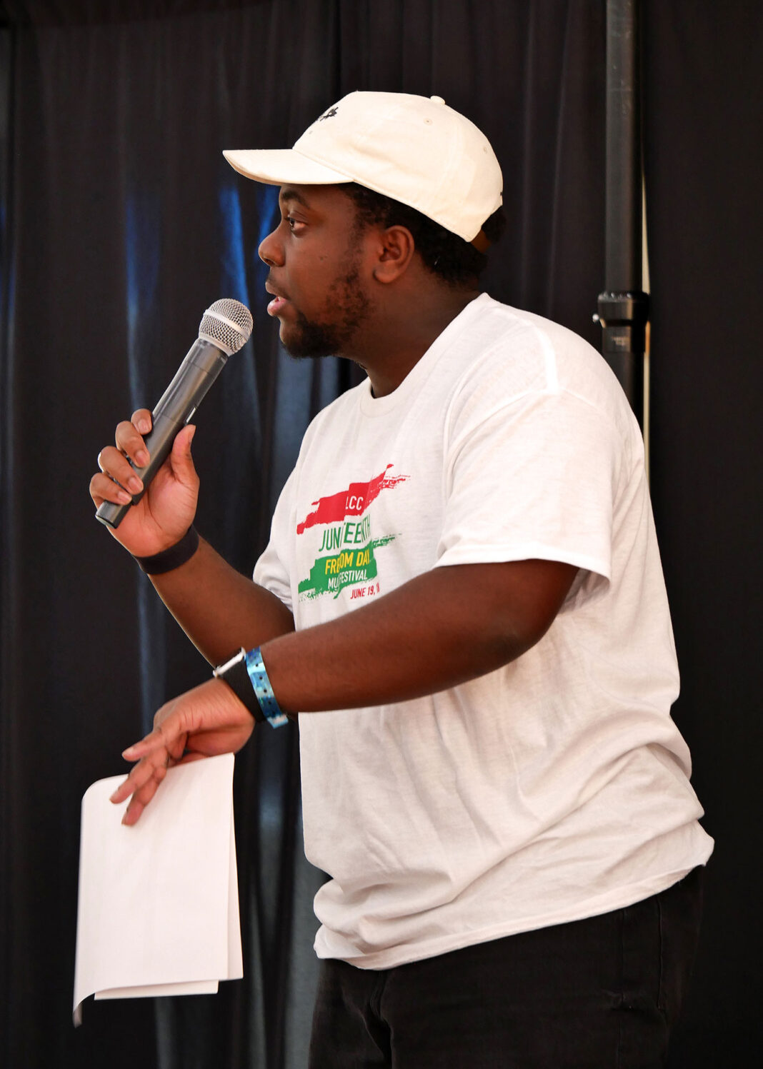 Simon Kalapokis wearing a white t-shirt and baseball cap and singing into a microphone