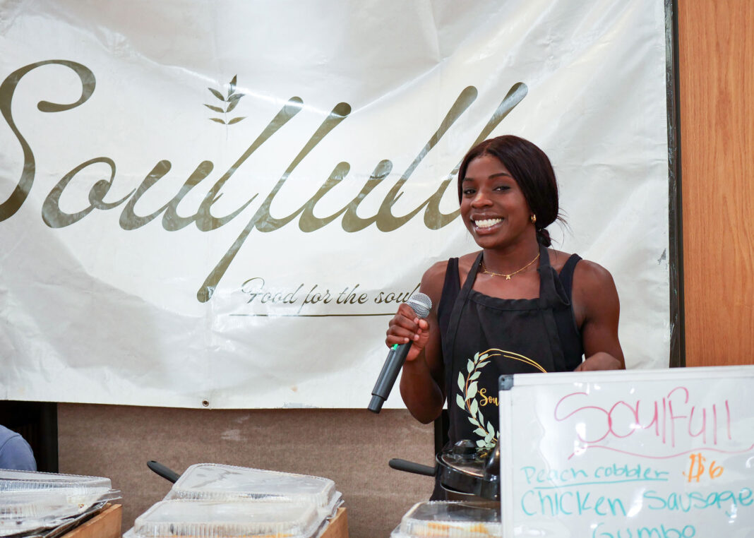 Alysa Whitney smiling and holding a microphone while tending to her vendor space