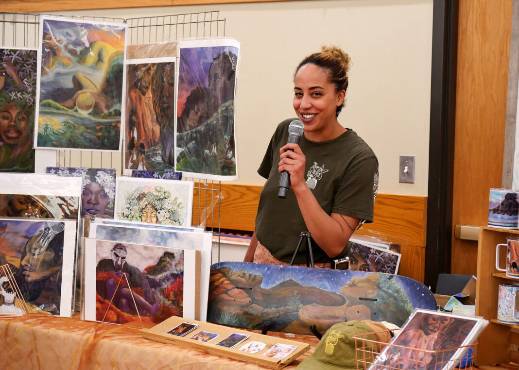 Graclynn Hucommpo holding a microphone while tending to her vendor area