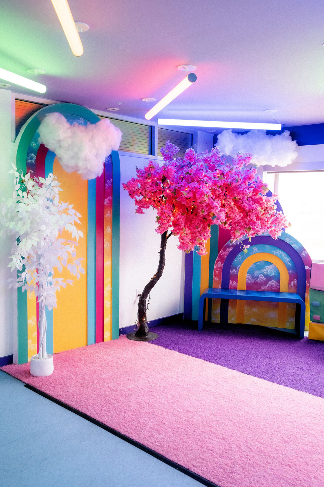 A multicolored- room with a pink tree, halogen lights and rainbows
