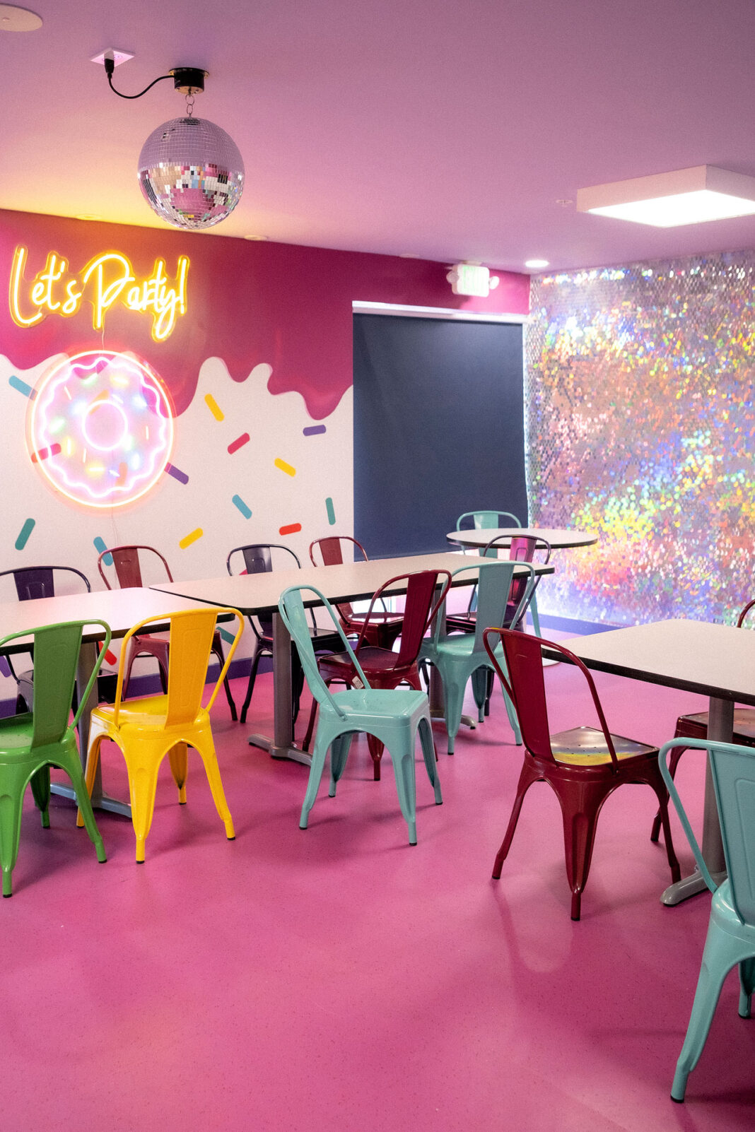 Neon sign reads "Let's Party!" on a wall next so tables and chairs and a crystal ball