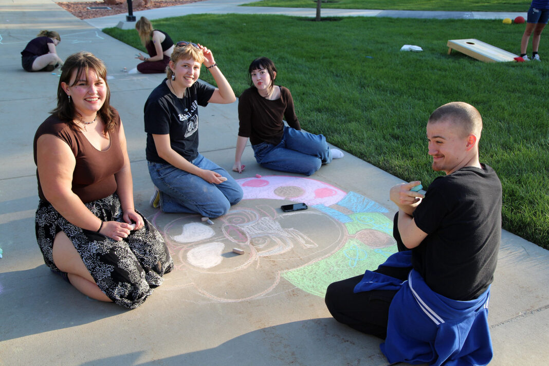 Four people contributing to a chalk art drawing