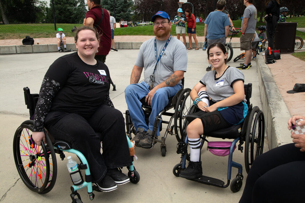 Three people using wheelchairs and visiting at a skate park