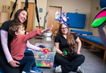 Supportive occupational therapy program administration assists in filling growing societal need Two therapists playing with a child who is practicing throwing an object to a target