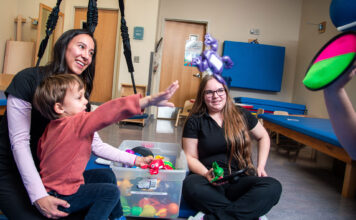 Supportive occupational therapy program administration assists in filling growing societal need Two therapists playing with a child who is practicing throwing an object to a target