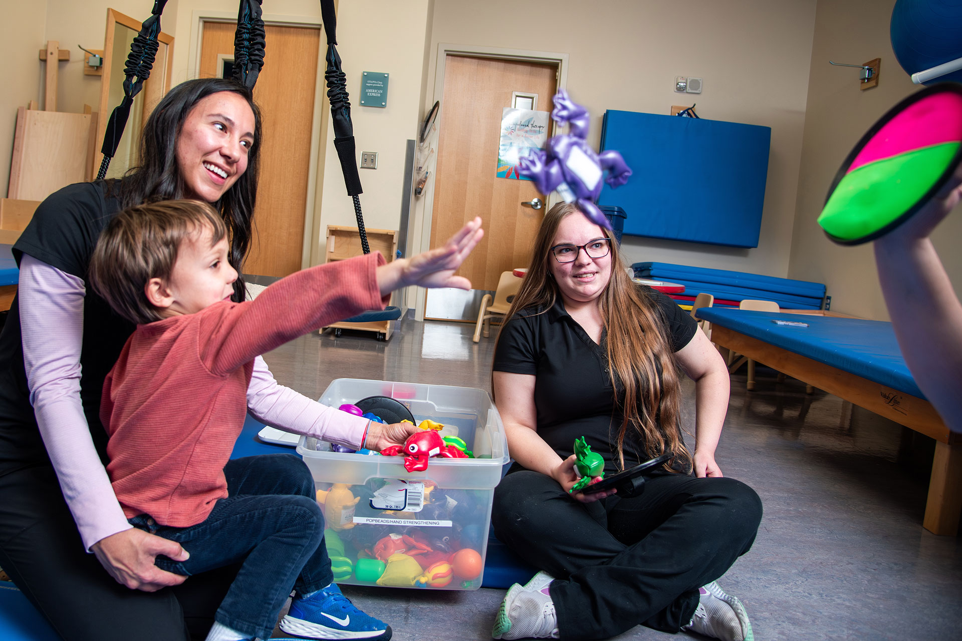 Two therapists playing with a child who is practicing throwing an object to a target.