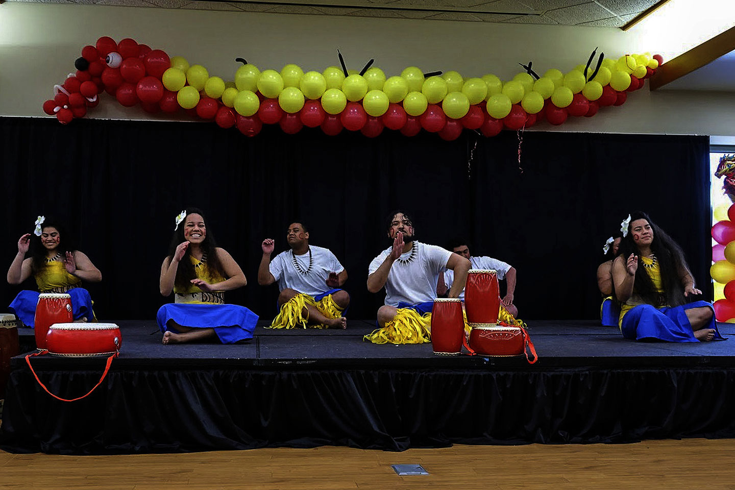 Pacific Islander men and women seated on a stage playing drums