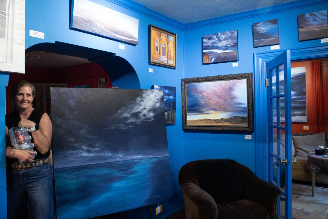 Anne holding bottled water in a blue painted room with paintings on display