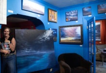 A beautiful art walk, nestled in the Avenues Anne holding bottled water in a blue painted room with paintings on display