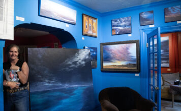 A beautiful art walk, nestled in the Avenues Anne holding bottled water in a blue painted room with paintings on display