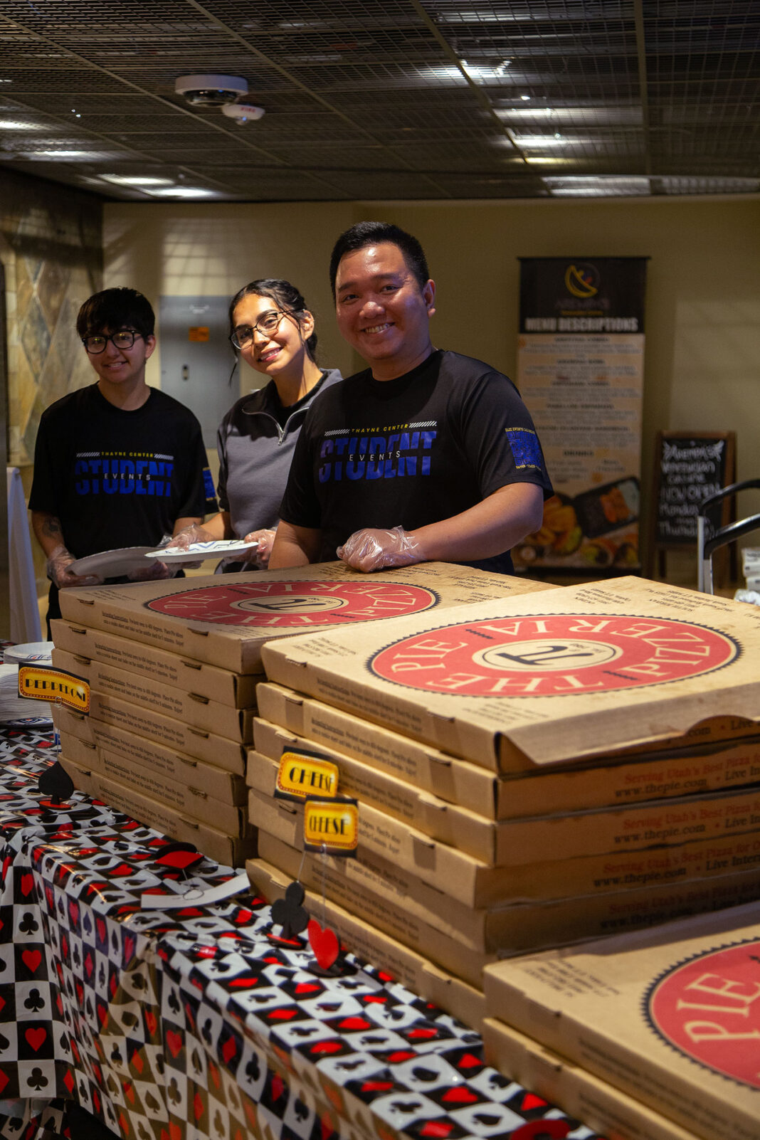 Three students working an event with boxes of pizza stacked on a table