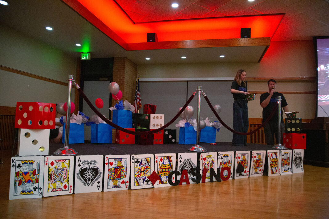 Two people standing with prizes on a stage decorated with playing cards on the front