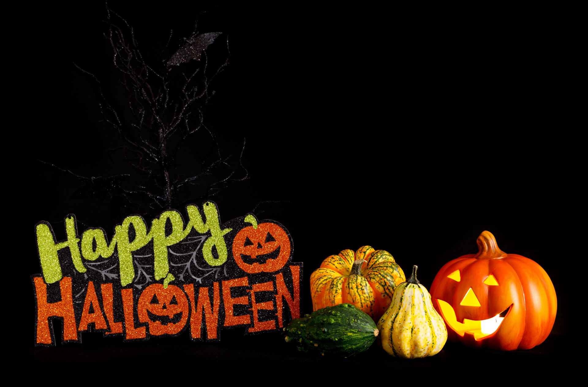 Happy Halloween text with gourds of various shapes and colors on a black background