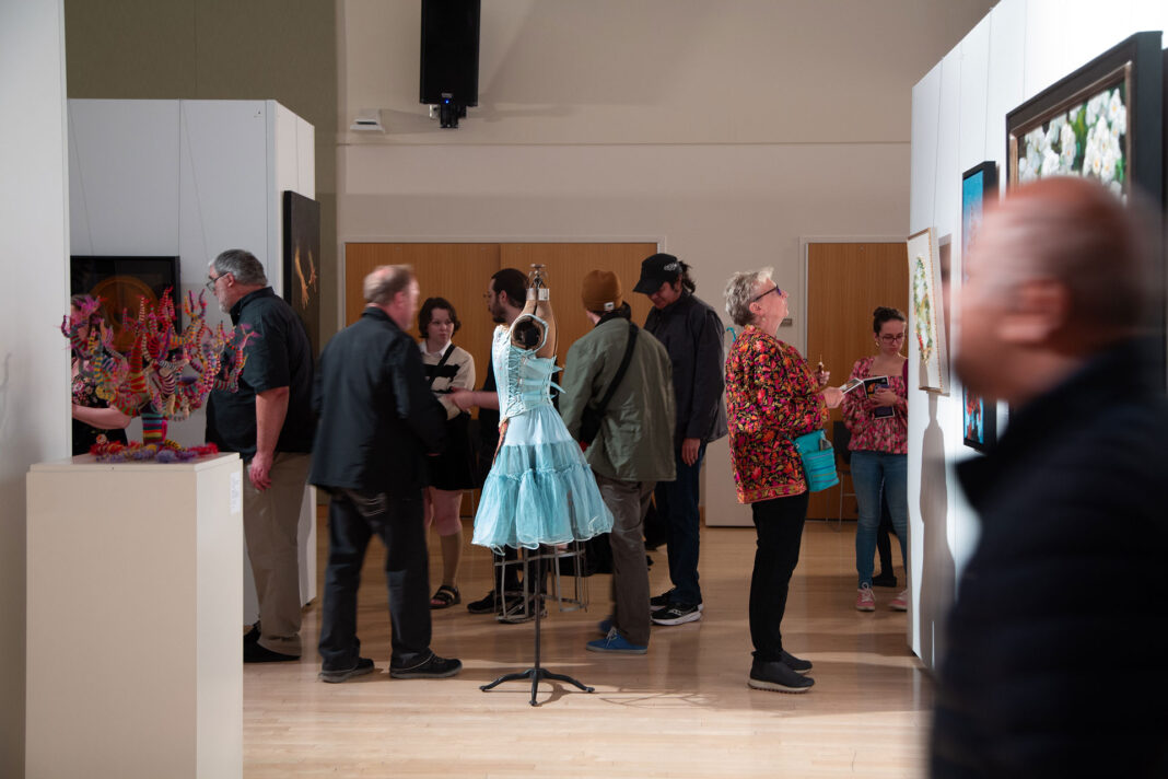 Several people looking at art exhibits in a multipurpose room