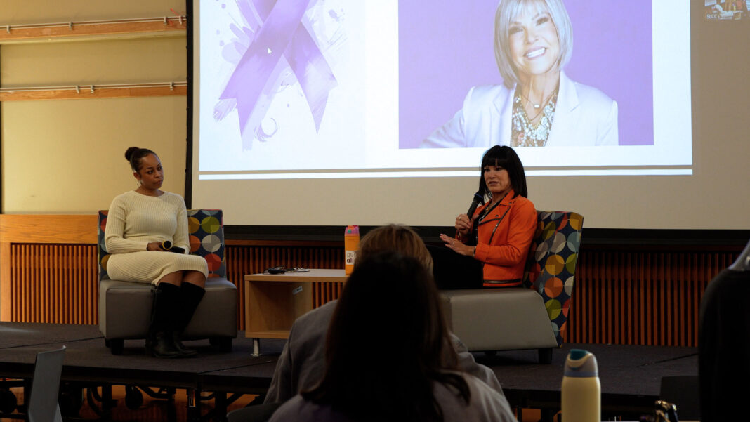 Mary, wearing a pink jacket, sharing her story while sitting on a riser with Chenoa