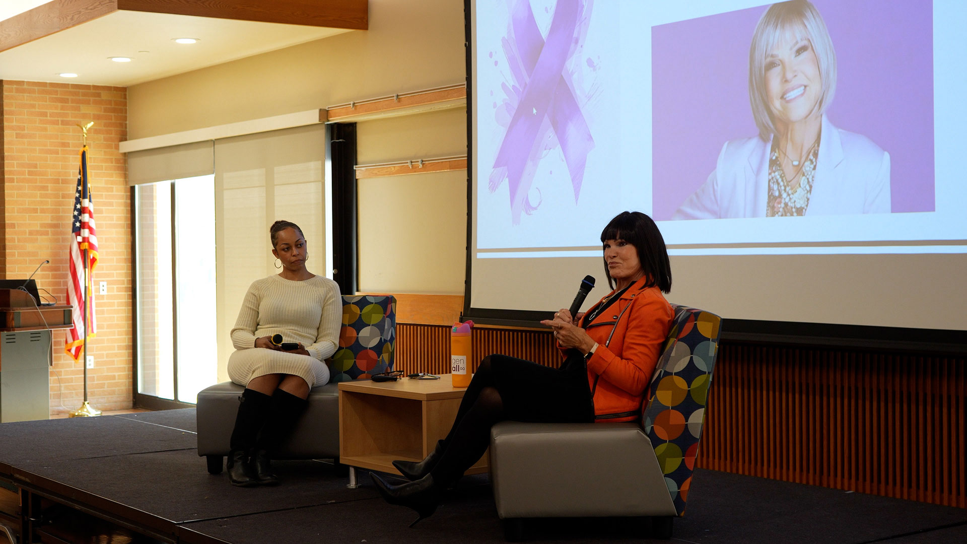 Mary, wearing a pink jacket, sharing her story while seated on stage with Chenoa
