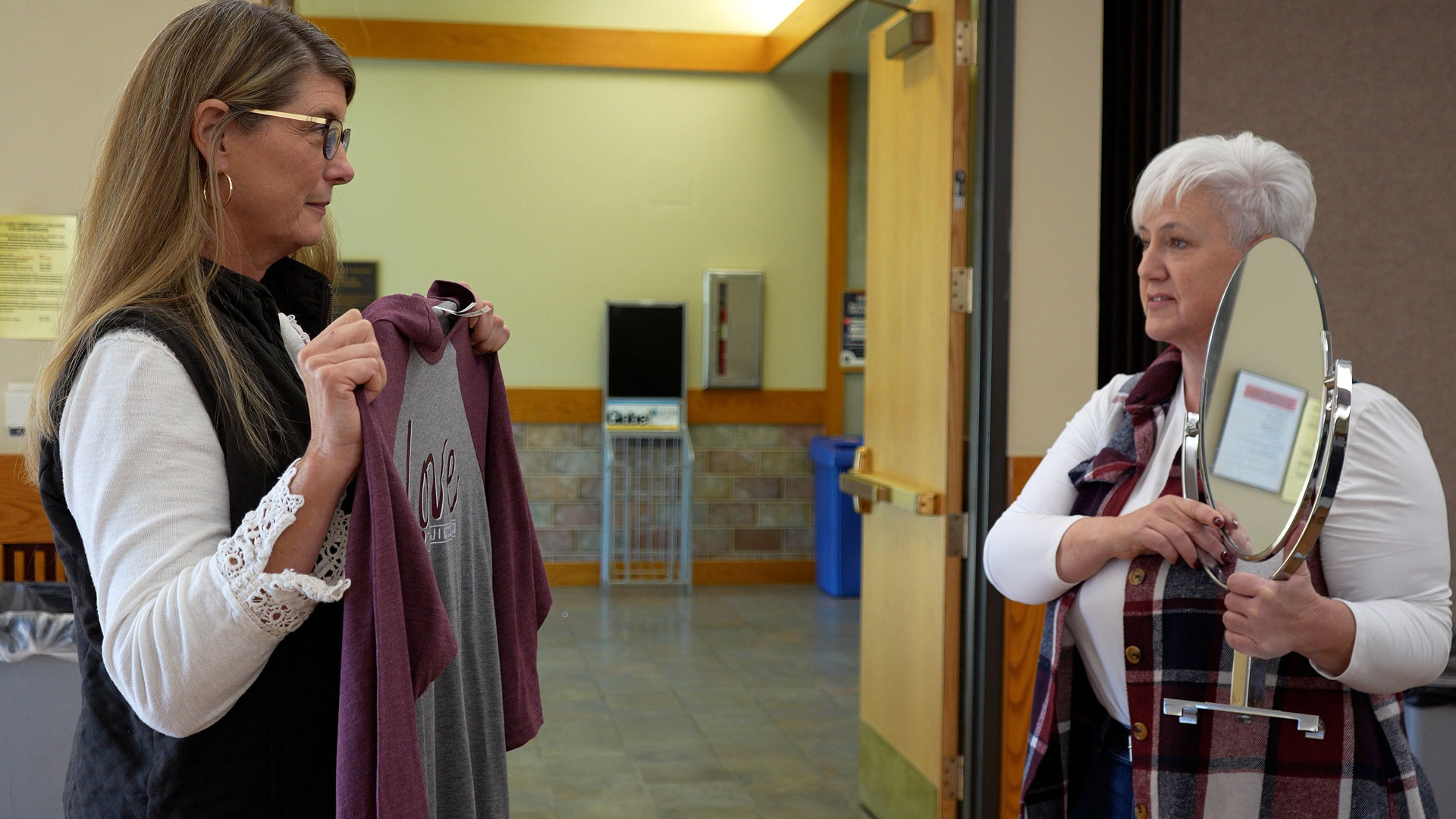 Penny holding a shirt while Lori holds a mirror