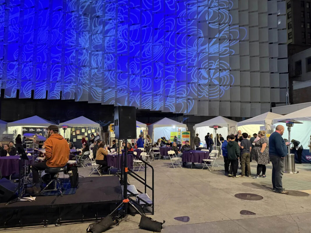 People walking and visiting information booths on a plaza at night